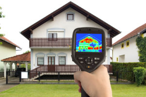 Home inspector outside looking at a home with a thermal image camera.